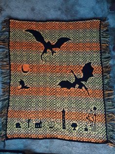 an orange and black knitted blanket with bats flying over the city at night time