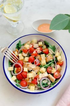 a salad with chicken, tomatoes, onions and cheese in a blue and white bowl