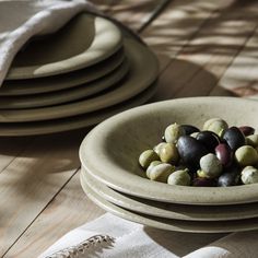 a bowl filled with olives sitting on top of a wooden table next to plates