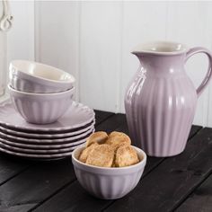 a table topped with plates and bowls filled with food next to a pitcher on top of a wooden table