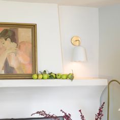 a painting is hanging on the wall next to a fire place with apples and flowers