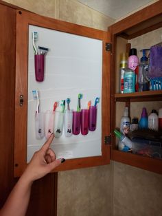 a person pointing at toothbrushes on a wall mounted to a cabinet in a bathroom