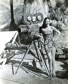 a woman standing in front of an old fashioned movie camera on a wooden tripod