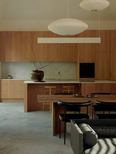 an open kitchen and living room with wooden cabinets, black leather couches and white lamps hanging from the ceiling