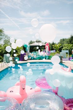 an inflatable flamingo float floating on top of a pool surrounded by balloons