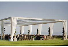 an outdoor wedding setup with white draping and flower arrangements on the grass area