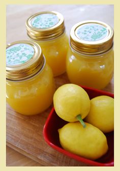 four jars filled with lemon curd sitting on top of a wooden table next to apples