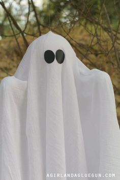 a white ghost hanging from a tree with black eyes