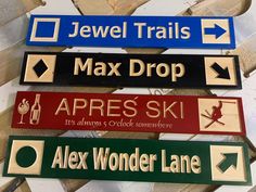 three different signs are hanging on the wall above wood planks that read jewel trails, max drop, apres ski, apex's ski and alex wonder lane