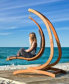 a woman is sitting on a wooden chair at the beach