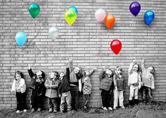 a group of children standing in front of a brick wall with balloons attached to it