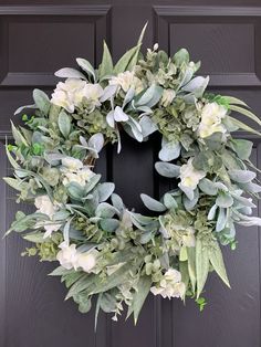 a wreath with white flowers and greenery is hanging on the front door's black frame