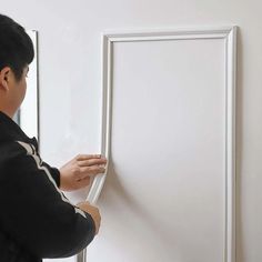 a man is painting a white frame on the wall with an adhesiver tape