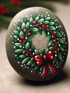 a painted rock with holly wreath on it and red bow tie around the neck, sitting on a table