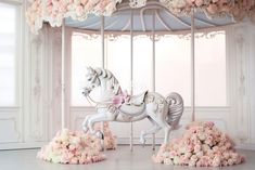 a white carousel with pink flowers on the ground and in front of it is a horse