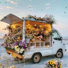 an ice cream truck is covered in flowers and lights on the beach with birds flying overhead