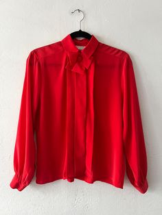 Bright red long sleeve silky collared button up with pleating on the front and a bow at the neckline that is held on with a bobby pin. Unlined with button sleeve cuffs. In excellent vintage condition. DETAILSLabel: Nicole Blake PetitesMaterial: 100% Polyester SIZE & MEASUREMENTSTag Size: 6 Best Fits: XS/Small Length: 24"Bust: 38"Waist: 38"Sleeve: 22"Shoulder: 16" Includes Free US Shipping Red Collared Blouse For Fall, Red Collar Blouse For Work, Silk Formal Tops With Bow Detail, Red Collared Party Blouse, Red Long Sleeve Tops For Semi-formal Occasions, Formal Solid Color Tops With Bow, Formal Long Sleeve Tops With Bow Tie, Classic Long Sleeve Blouse With Bow, Classic Red Blouse For Fall