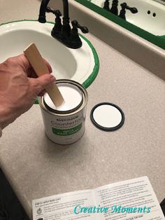 a person holding a brush over a paint can on a counter next to a sink