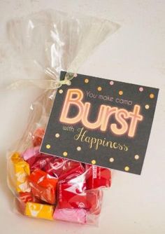 a bag filled with lots of candy sitting on top of a white table next to a sign that says burst with happiness