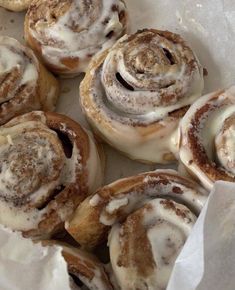 cinnamon rolls with icing sitting in a white paper wrapper on top of a table