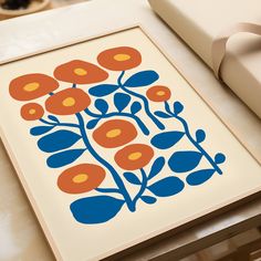 an orange and blue flower print on a white table next to a box with a brown ribbon