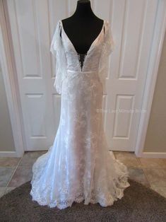 a white wedding dress on a mannequin in front of a door with an open back