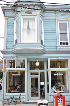 people are sitting at tables in front of a blue building with white trim and windows