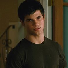 a young man in a black shirt is looking at the camera while standing next to a doorway