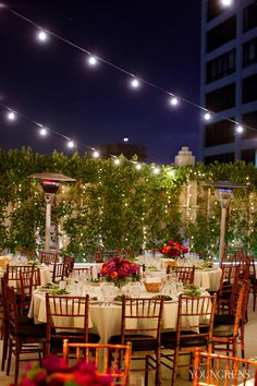 an outdoor dining area with tables and chairs, lights strung over the top of it