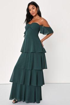 a woman wearing a green dress with tiered ruffles on the bottom and one shoulder