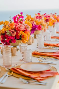 the table is set with orange, pink and yellow flowers in vases on each side