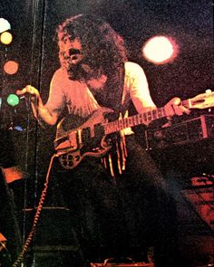 a man with long hair playing a guitar in front of microphones and lights on stage