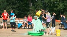 people are standing around in the park with buckets on their heads and one person is pouring water