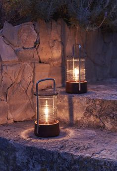 two lights that are sitting on some stone steps in front of a rock wall, one is lit up and the other is turned on