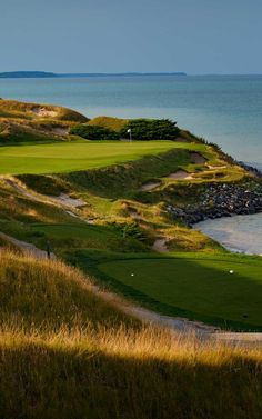 a golf course on the ocean with water in the background and sand dunes to the side