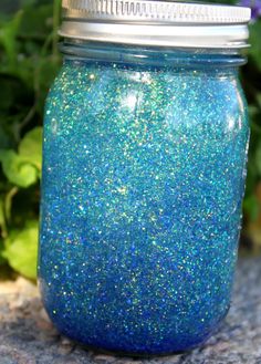 a blue and green jar sitting on top of a rock next to purple flowers in the background