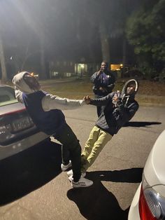 two people are dancing on the street in front of a car and another person is standing behind them