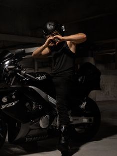 a man sitting on top of a motorcycle in a parking garage with his hand on the helmet