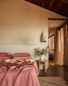 a bed with pink sheets and pillows in a bedroom next to a wooden ceiling fan