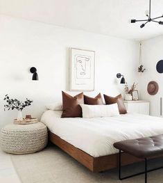 a white bed with brown pillows in a bedroom next to a plant on the wall