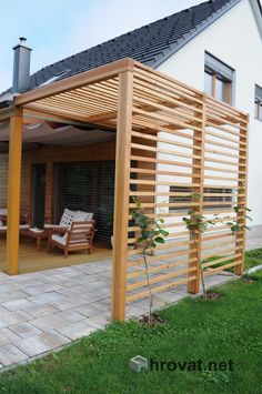 a wooden pergolated patio with chairs on the grass and an outdoor living area in the background