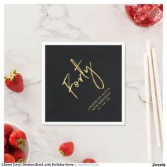 a black card with gold lettering and strawberries next to it on a marble surface