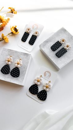 three pairs of black and white earrings with polka dots on them, sitting next to flowers