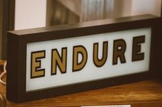 a sign with the word endure on it sitting on a wooden table in front of a mirror