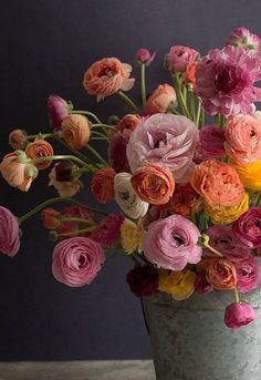 a vase filled with lots of different colored flowers on top of a wooden table next to a gray wall