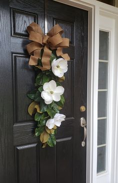 a black door with a brown bow and white flowers hanging on it's side