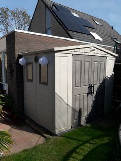 an outdoor storage shed with solar panels on the roof and windows, in front of a house