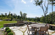 an outdoor table and chairs on a stone patio with trees in the backgroud