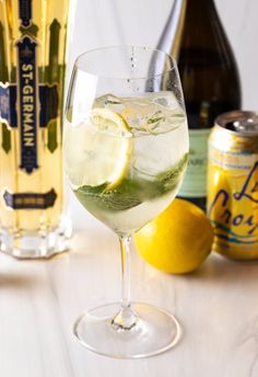 a glass filled with ice and water next to two bottles of wine, lemons and beer