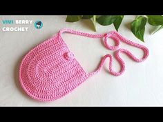 a pink crocheted purse sitting on top of a white table next to green leaves